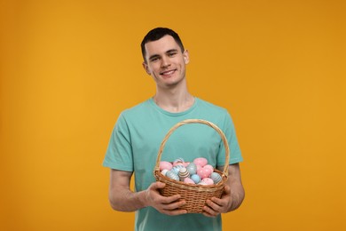 Photo of Easter celebration. Handsome young man with basket of painted eggs on orange background