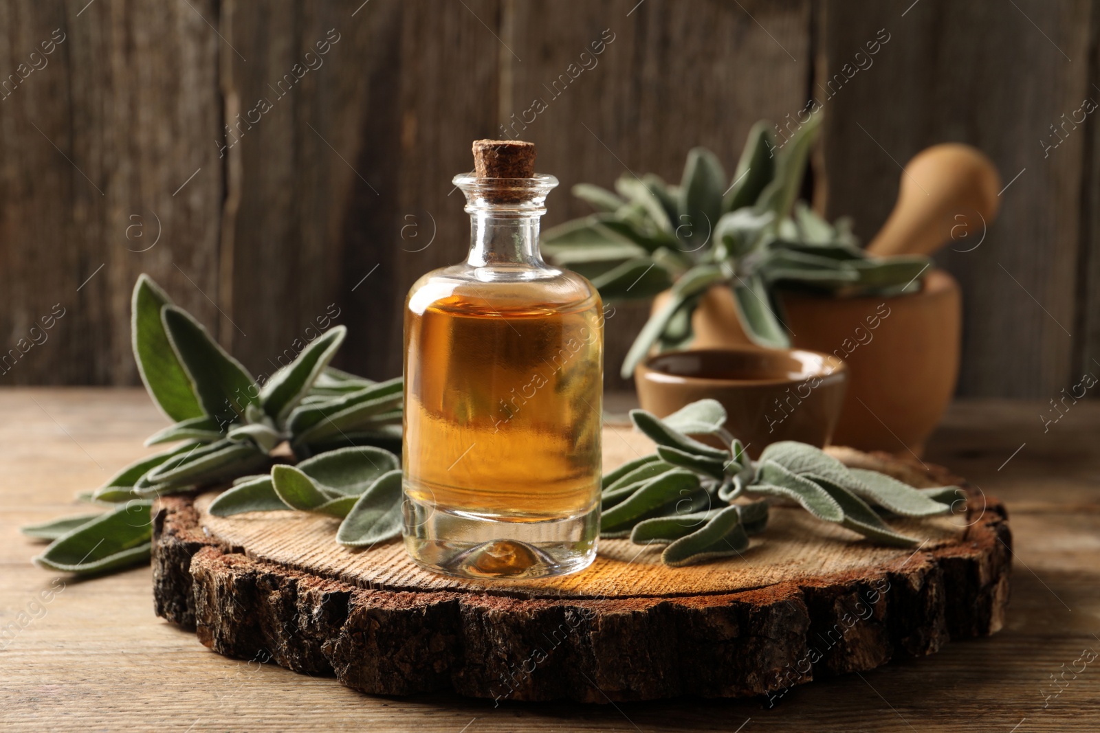 Photo of Bottle of essential sage oil and twigs on wooden table