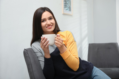 Photo of Young woman with cup of drink relaxing at home
