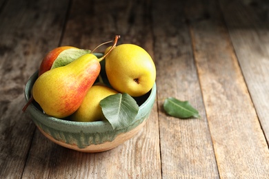 Photo of Bowl with ripe pears on wooden table. Space for text