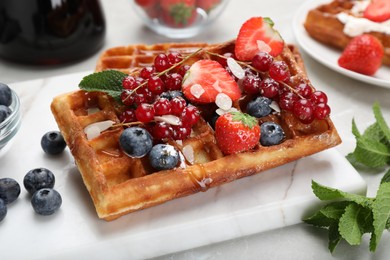 Photo of Board with delicious Belgian waffles, berries and caramel sauce on table, closeup