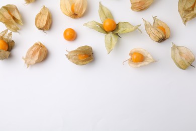 Ripe physalis fruits with calyxes on white background, flat lay. Space for text