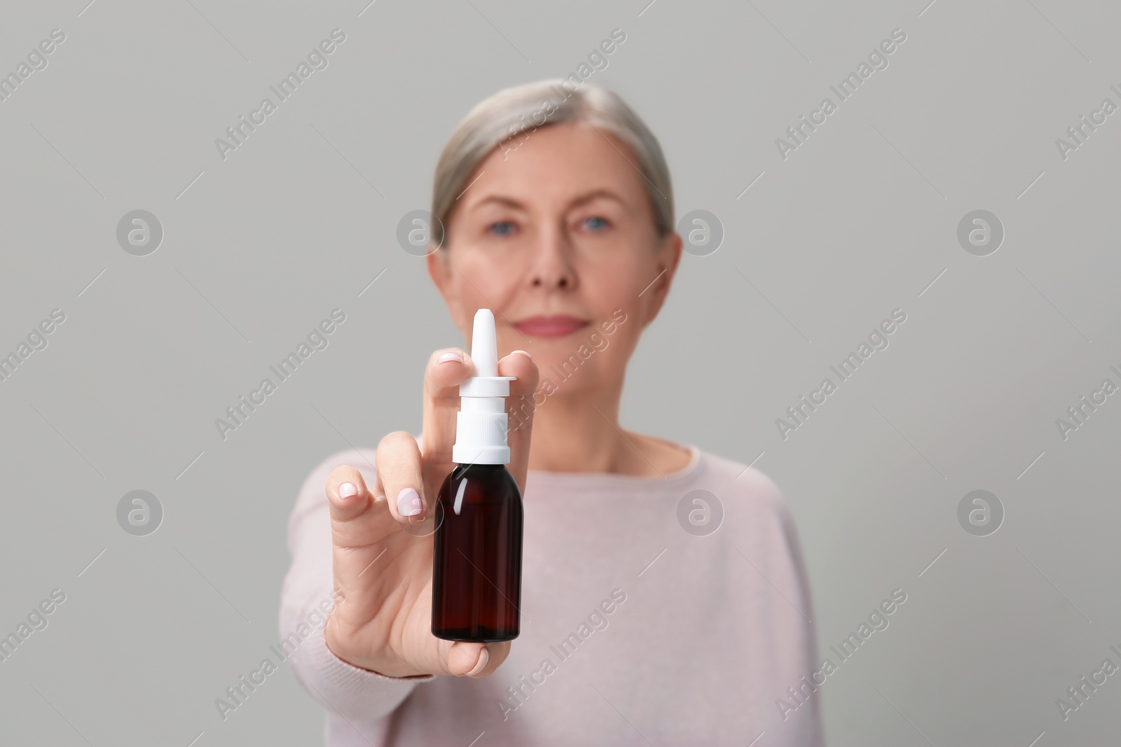 Photo of Woman holding nasal spray against light grey background, focus on bottle