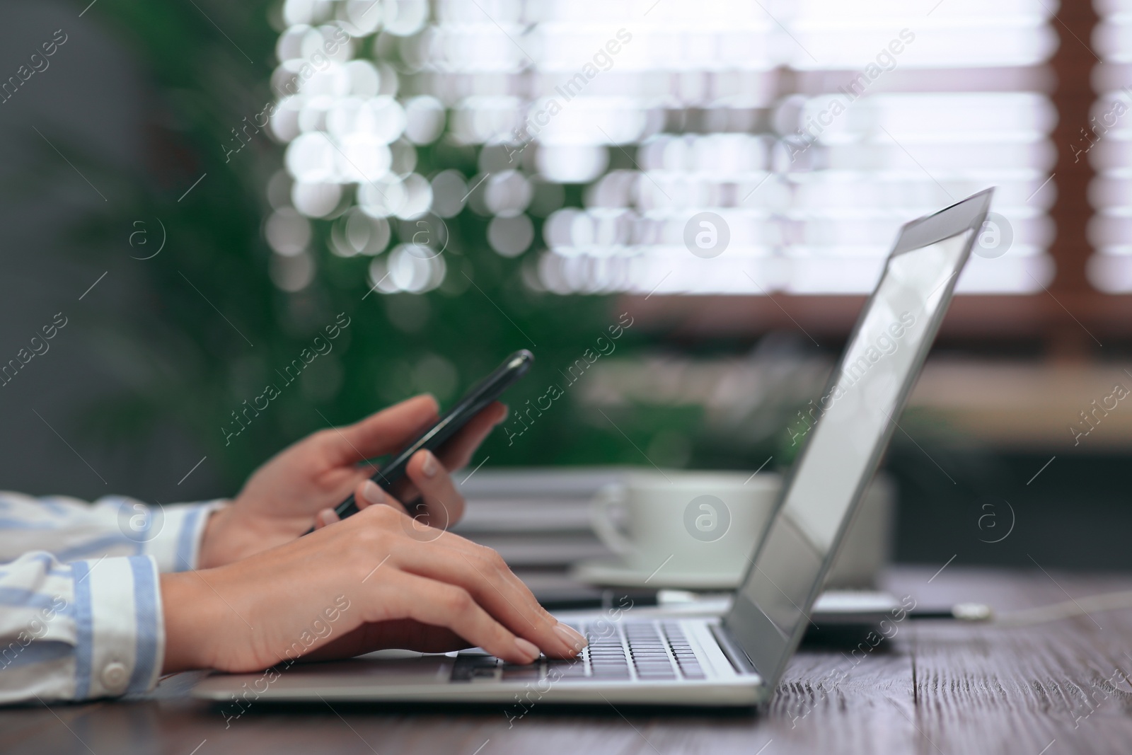 Photo of Woman with mobile phone working on modern laptop at table, closeup