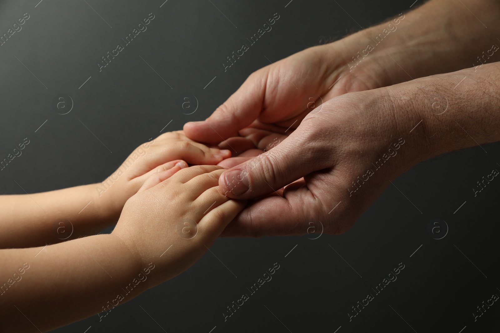 Photo of Father and child holding hands on dark grey background, closeup