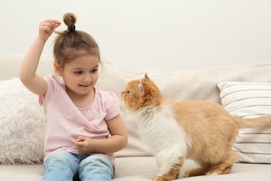 Photo of Happy little girl with cute cat on sofa at home