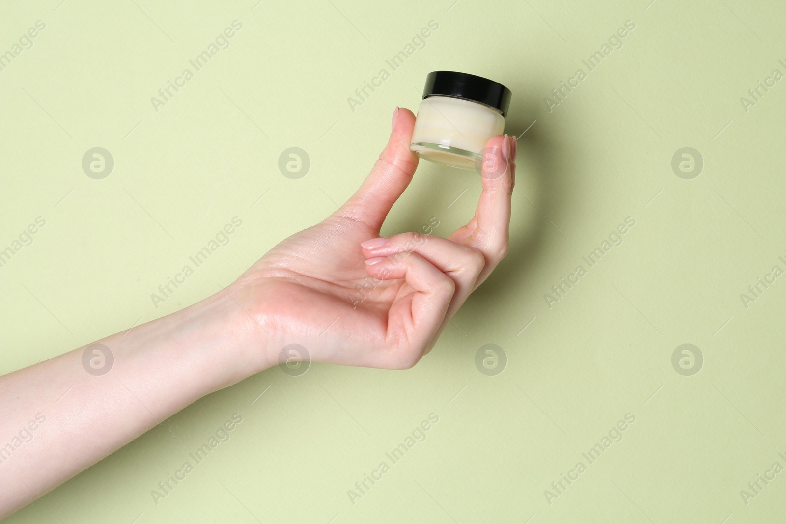 Photo of Woman holding jar of cream on green background, closeup