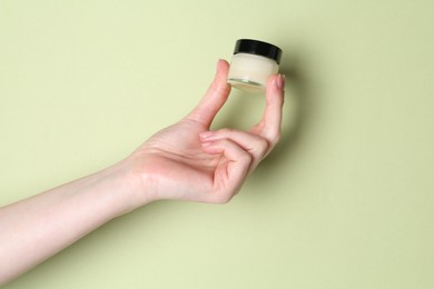 Woman holding jar of cream on green background, closeup