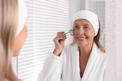 Woman massaging her face with metal roller near mirror in bathroom