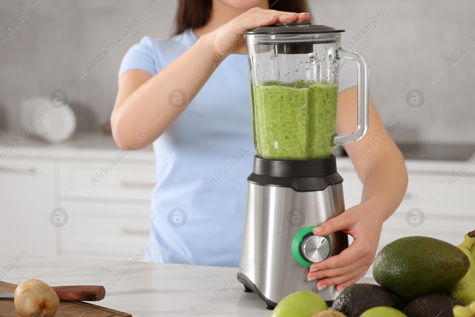 Photo of Woman preparing tasty smoothie at white table in kitchen, closeup