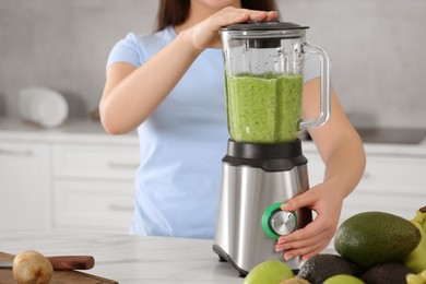 Woman preparing tasty smoothie at white table in kitchen, closeup