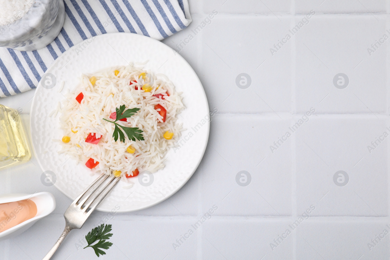 Photo of Delicious rice with vegetables and parsley served on white tiled table, flat lay