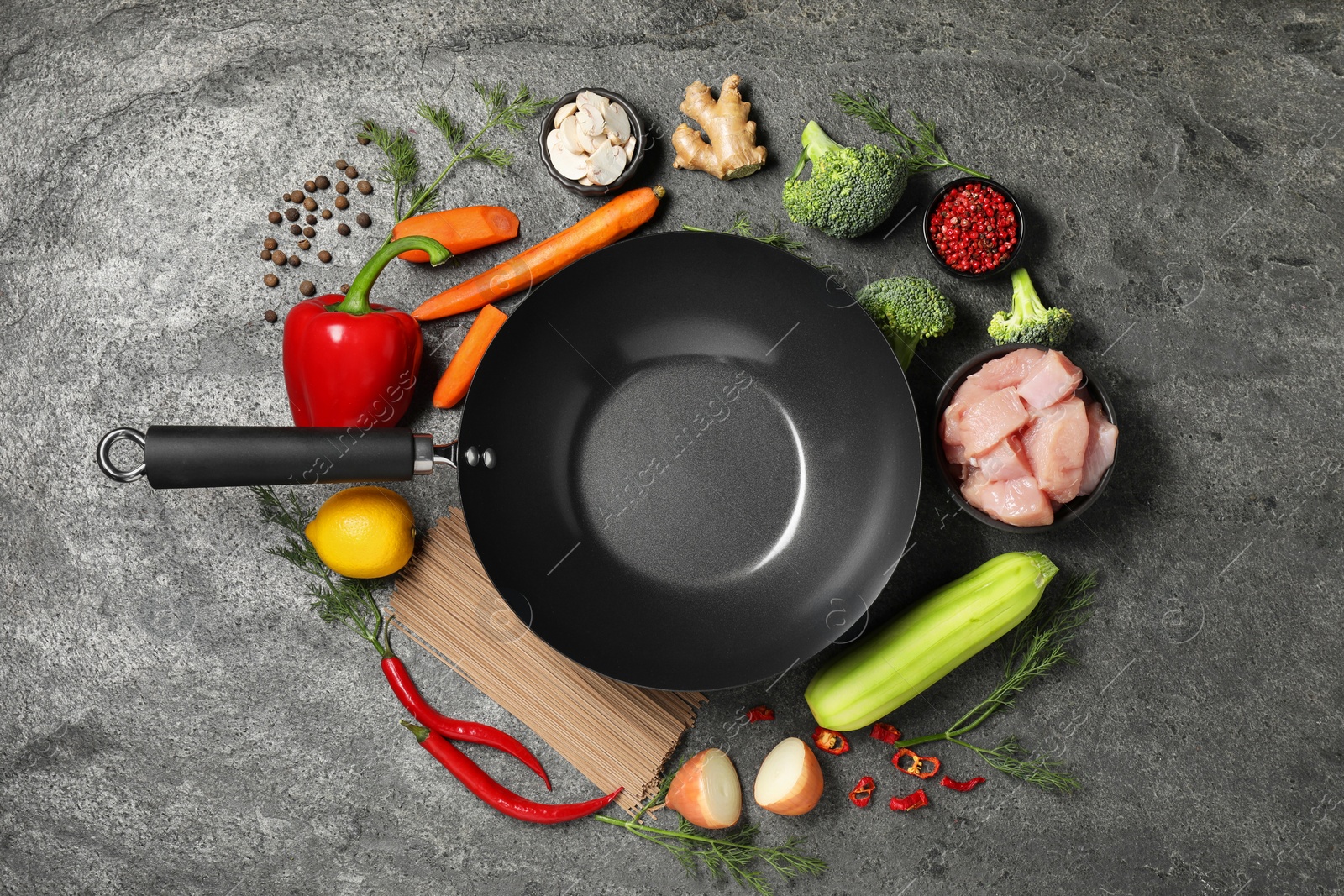 Photo of Empty iron wok surrounded by raw ingredients on grey table, flat lay