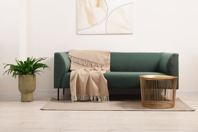 Photo of Stylish living room interior with comfortable sofa, blanket, houseplant and side table