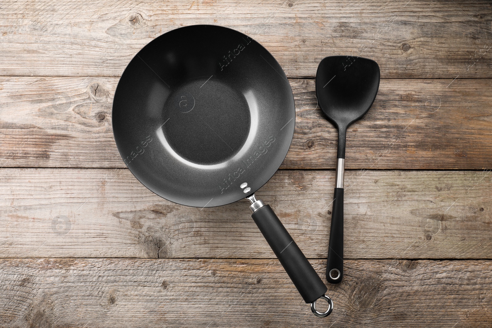 Photo of Black metal wok and spatula on wooden table, top view