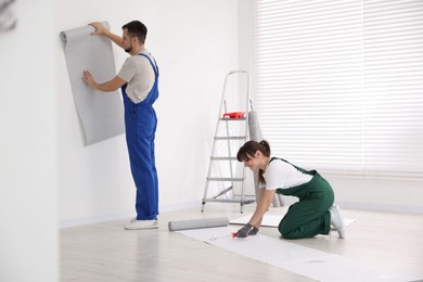 Woman applying glue onto wallpaper while man hanging sheet indoors