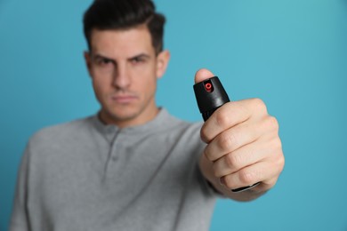 Photo of Man using pepper spray against turquoise background, focus on hand