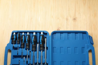 Photo of Set of screwdrivers in open toolbox on light wooden table, top view. Space for text