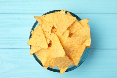 Photo of Glass bowl of tasty Mexican nachos chips on light blue wooden background, top view