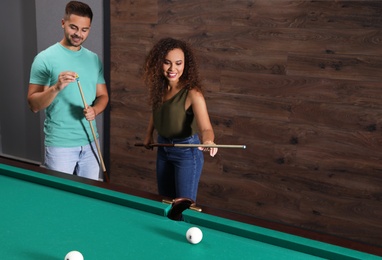 Young man and woman playing billiard indoors