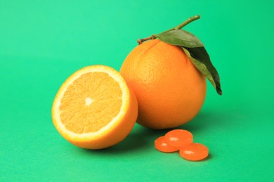 Photo of Cough drops and fresh oranges on green background