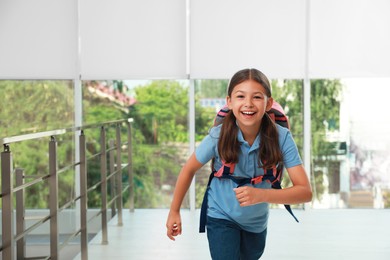 Photo of Happy little girl with backpack running in school, space for text