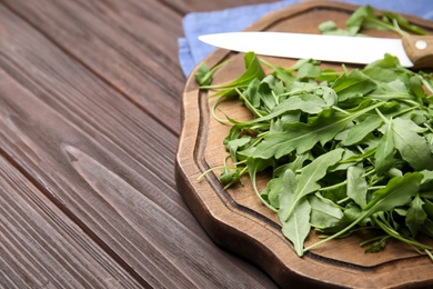 Photo of Cutting board with fresh arugula leaves and knife on wooden table, closeup. Space for text