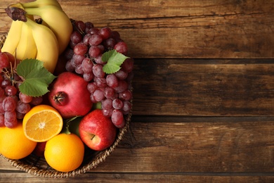 Wicker basket with different fruits on wooden table, top view. Space for text