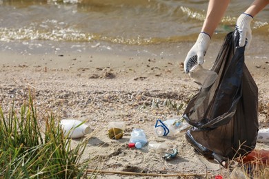 Photo of Woman in gloves with trash bag collecting garbage on beach, closeup