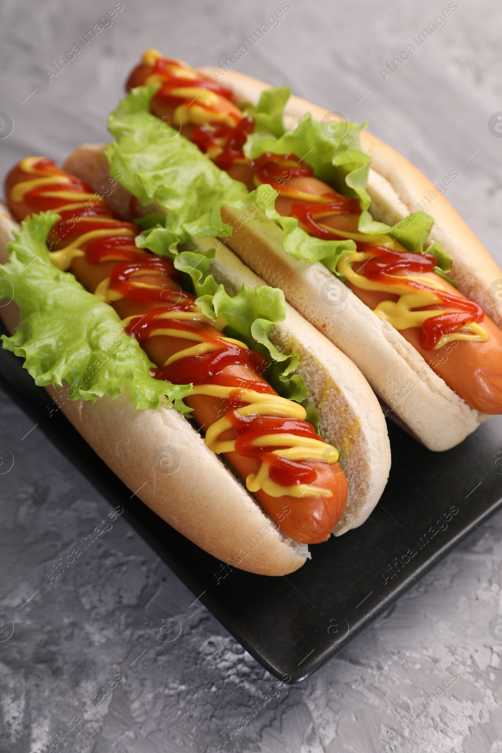 Photo of Tasty hot dogs with lettuce, ketchup and mustard on grey textured table, closeup