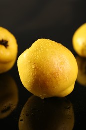 Photo of Tasty ripe quinces with water drops on black mirror surface, closeup