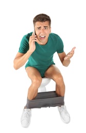 Young man with mobile phone sitting on toilet bowl. Isolated on white