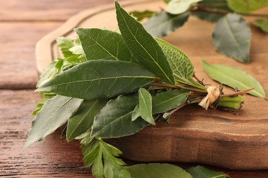 Aromatic fresh bay leaves and different herbs on wooden table, closeup