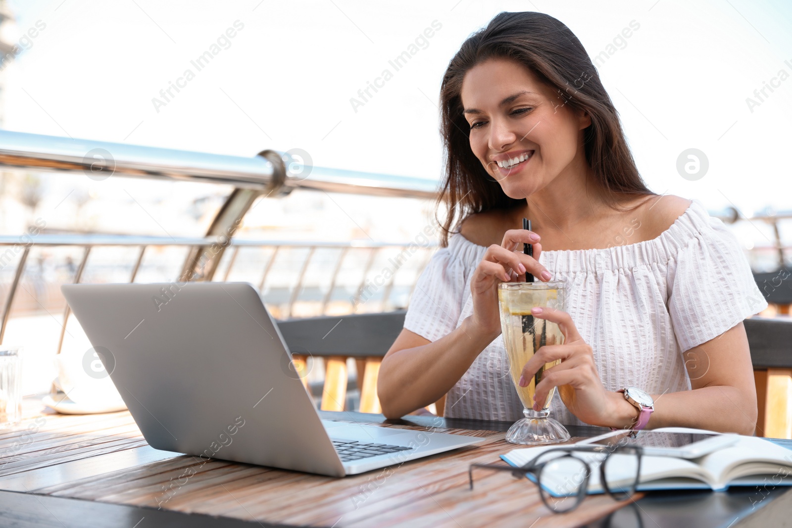 Photo of Beautiful woman with refreshing drink and laptop at outdoor cafe