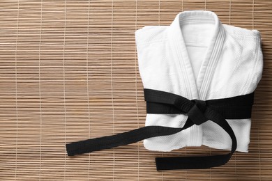 Photo of Martial arts uniform with black belt on bamboo mat, top view. Space for text