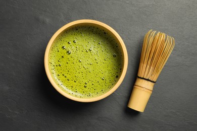 Cup of fresh matcha tea and bamboo whisk on black table, flat lay