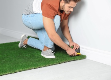 Man cutting artificial grass carpet at home