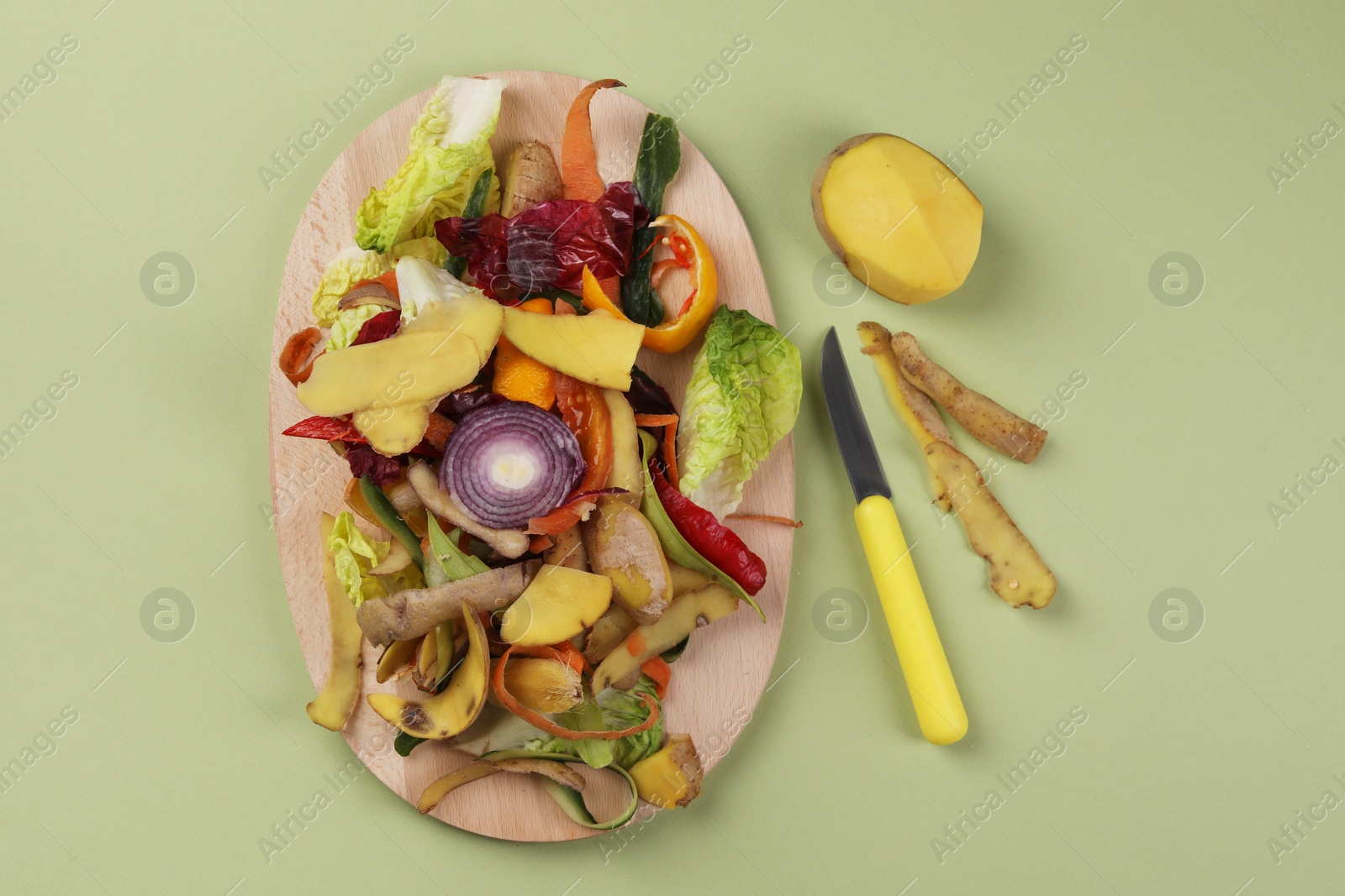 Photo of Peels of fresh vegetables and knife on light green background, flat lay