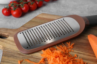 Hand grater and fresh ripe carrot on wooden board, closeup