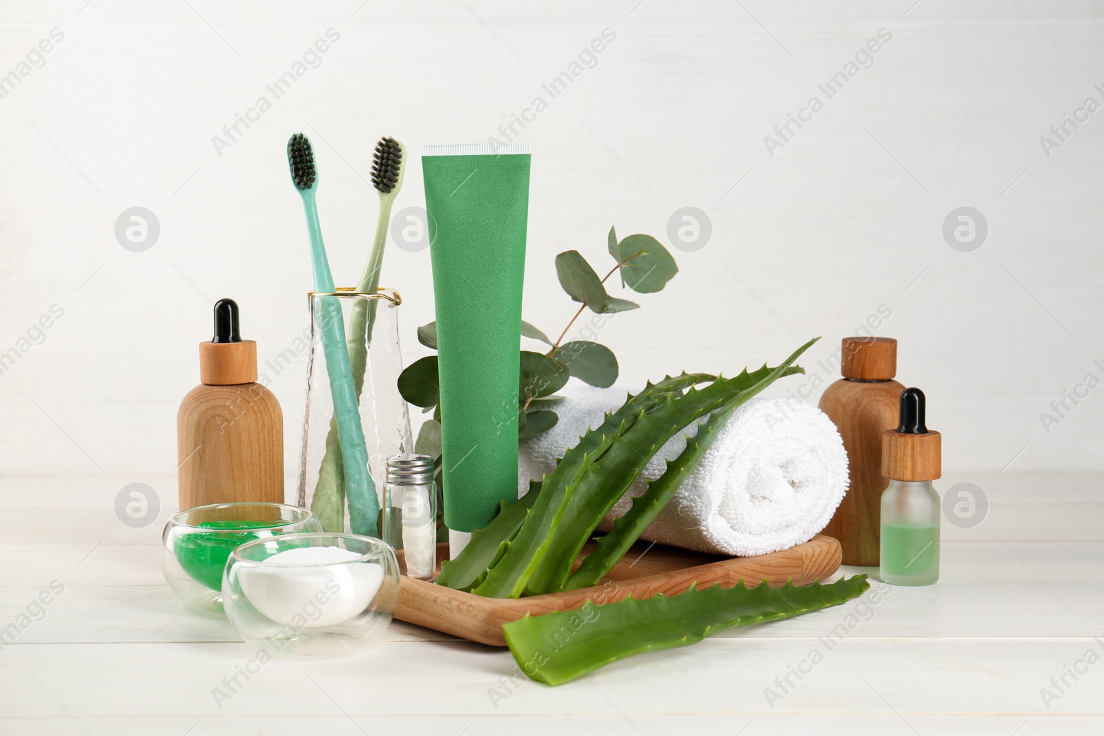 Photo of Tube of toothpaste, toothbrushes, fresh aloe, eucalyptus leaves and care products on white wooden table