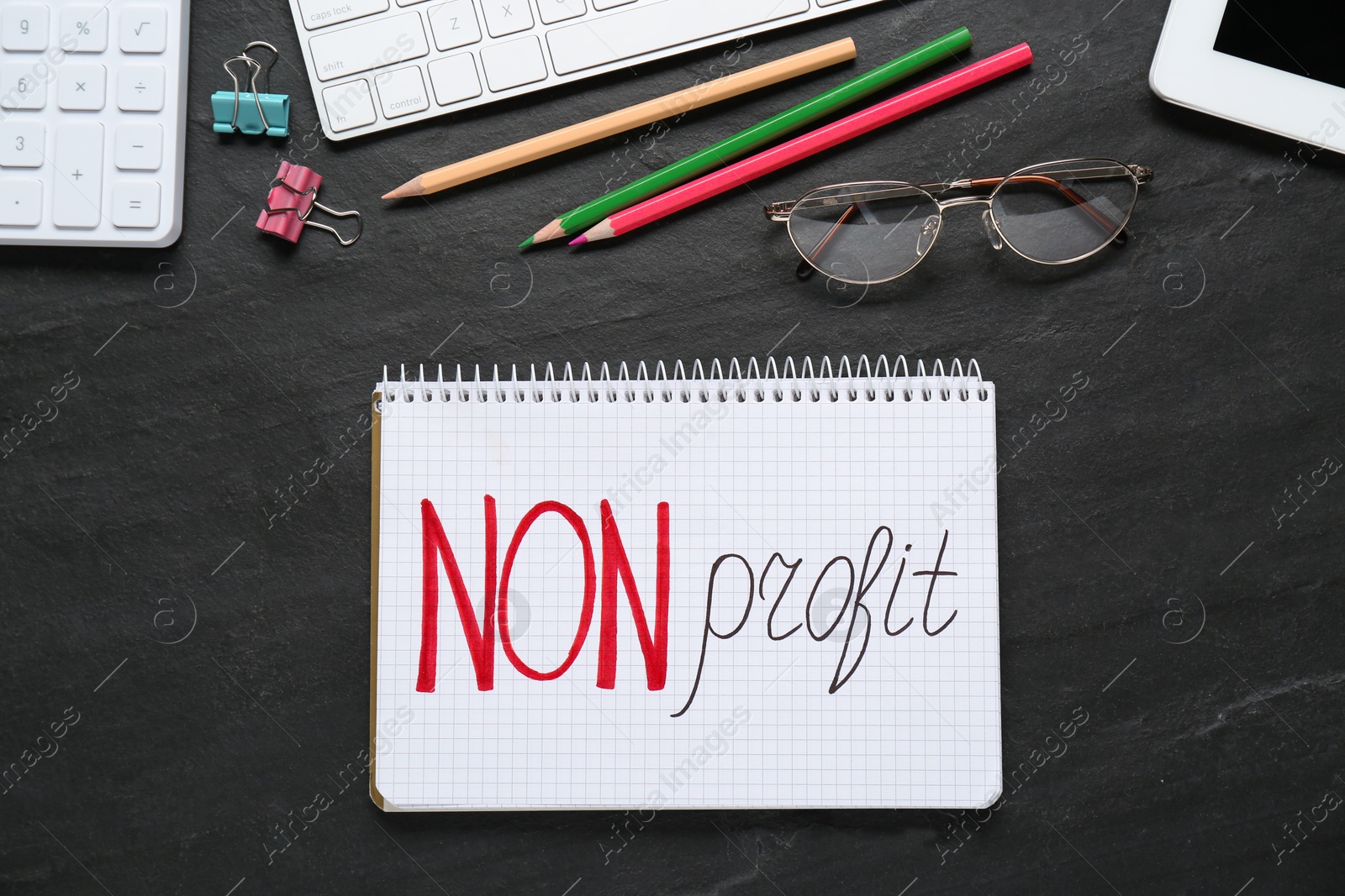 Photo of Notebook with phrase Non Profit, stationery and glasses on black table, flat lay