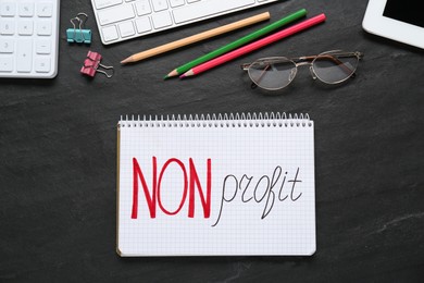 Photo of Notebook with phrase Non Profit, stationery and glasses on black table, flat lay