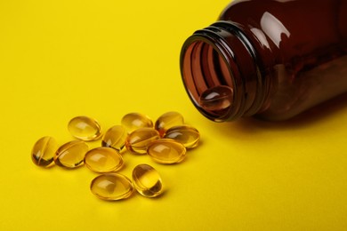 Overturned bottle with dietary supplement capsules on yellow background, closeup