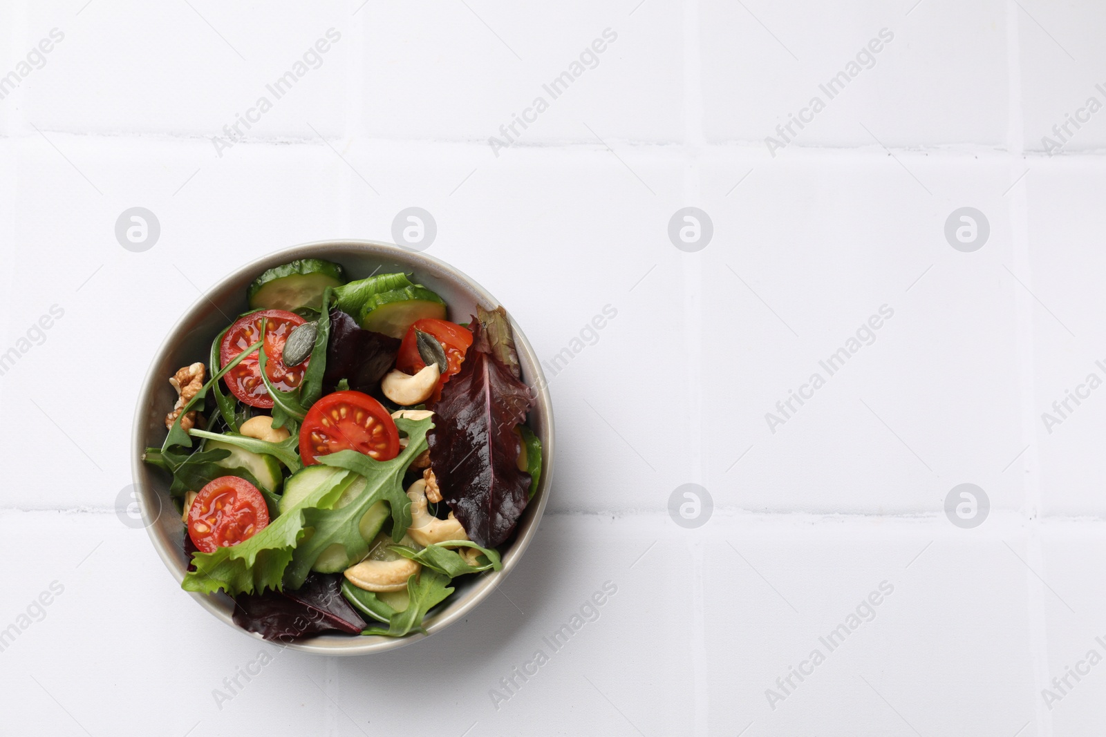 Photo of Tasty fresh vegetarian salad on white tiled table, top view. Space for text