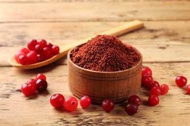 Cranberry powder in bowl and fresh berries on wooden table, closeup