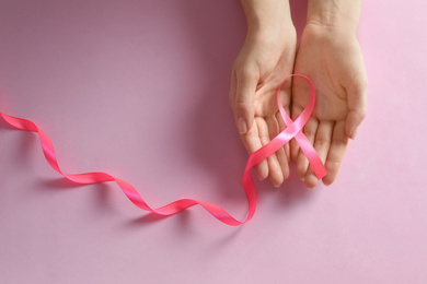 Woman holding pink ribbon on color background, top view. Breast cancer awareness