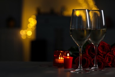 Photo of Glasses of white wine, burning candles and rose flowers on grey table against blurred lights, space for text. Romantic atmosphere