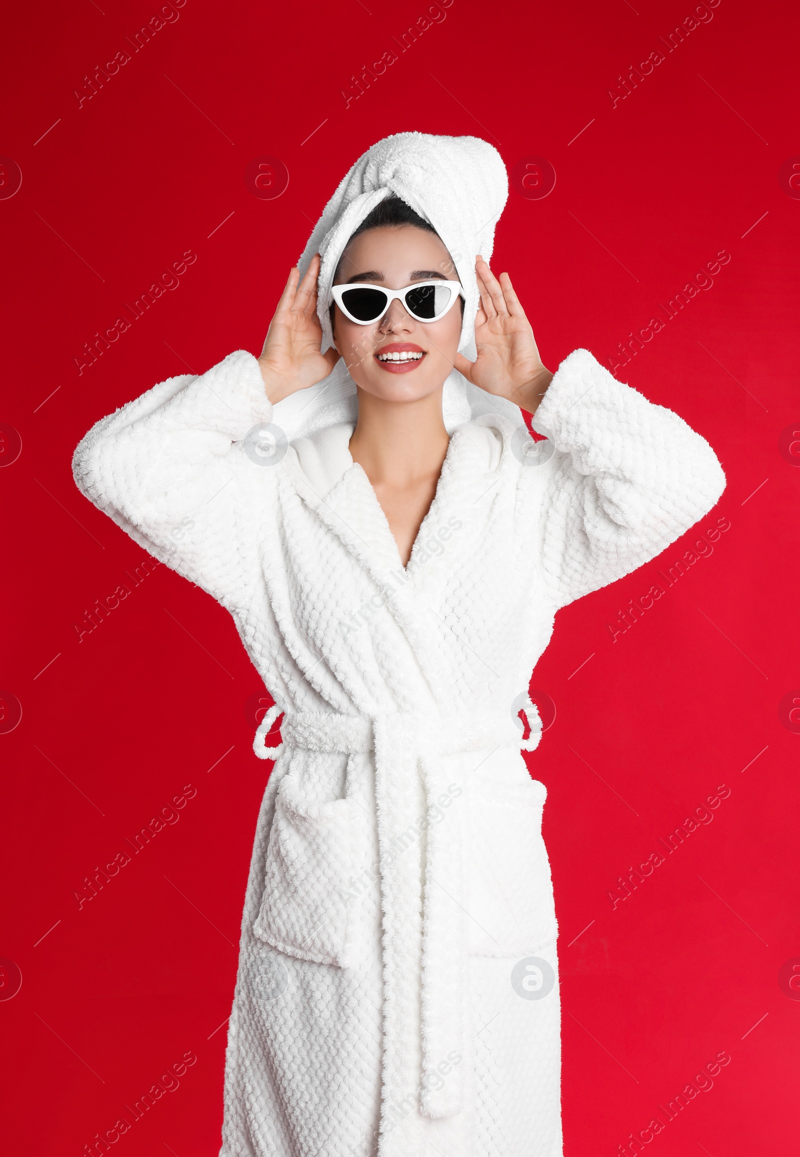 Photo of Beautiful young woman in bathrobe and sunglasses on red background