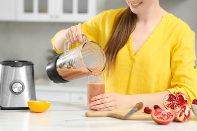 Photo of Woman pouring tasty smoothie into glass at white table in kitchen, closeup