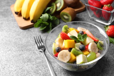 Photo of Delicious fresh fruit salad in bowl on grey table, space for text